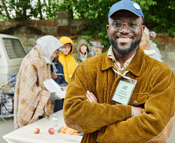 Smiling volunteer stands proudly in front of a table where other volunteers are working.