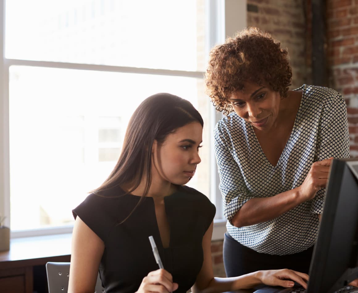 Two people helping one another on the computer. 