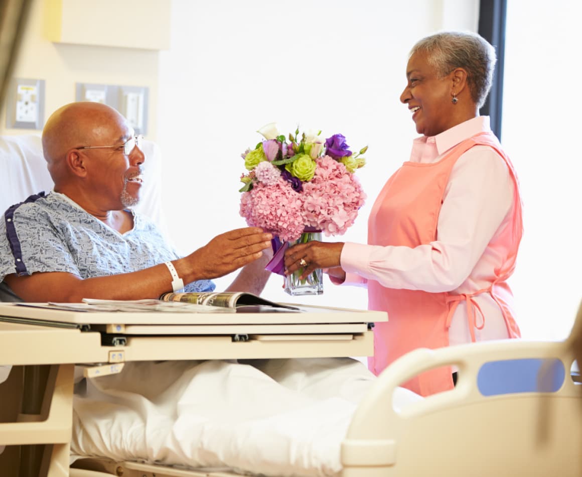 Woman giving man flowers in the hospital. 