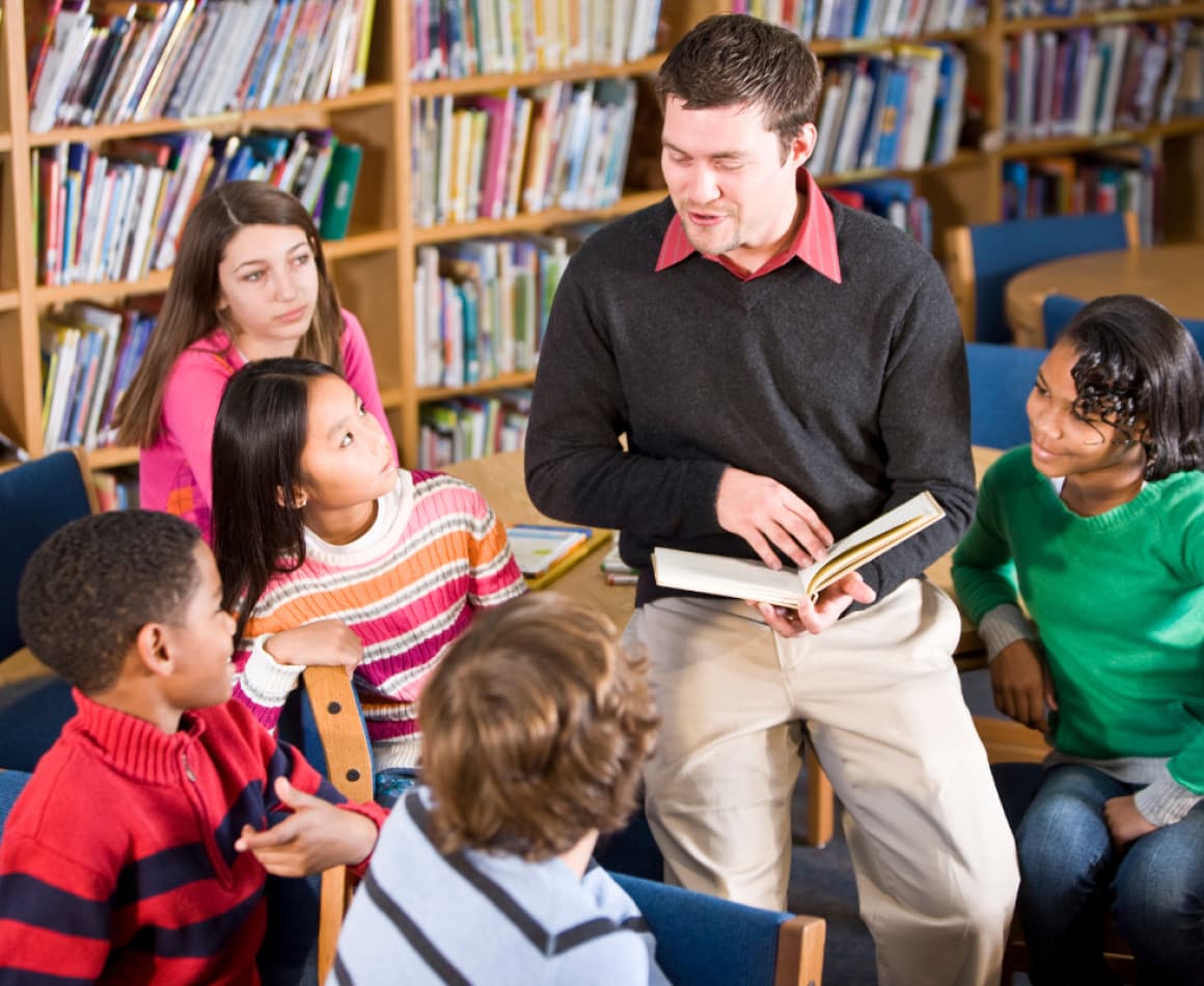 Librarian reading to kids in a library full of books. 