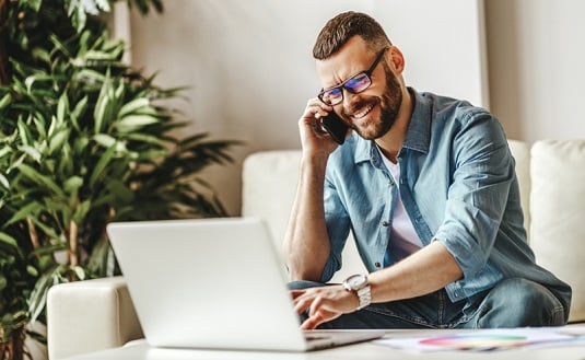 man talking on a cell phone while using a laptop