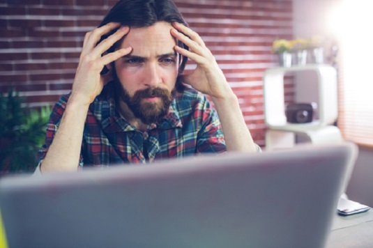 man holding his head in pain using a laptop